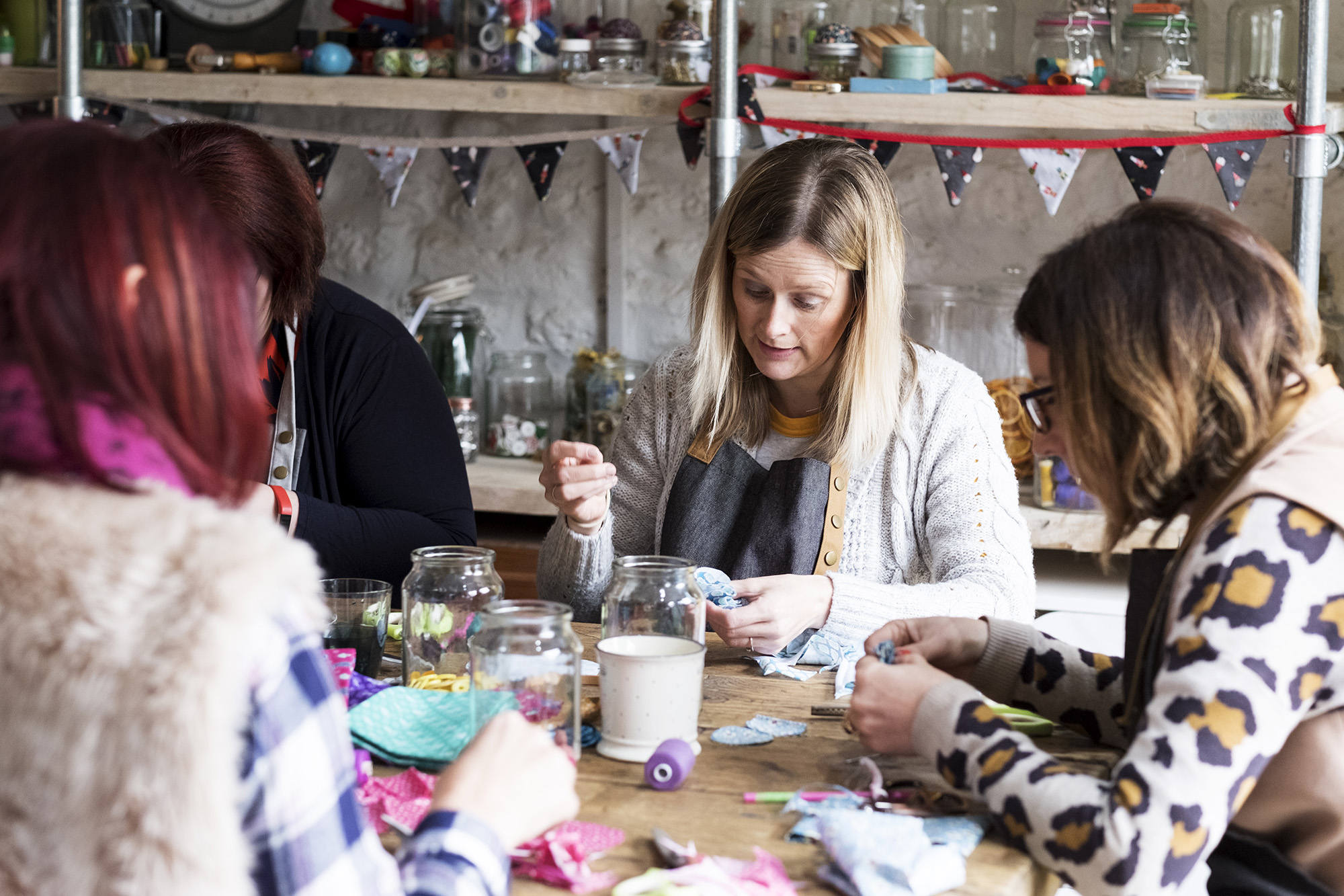 United Kingdom,Group of women sitting around a table in a workshop, making fabric flowers.